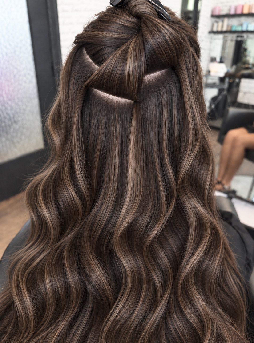 Back of long brown hair with a section lifted to show an Invisible Bead Extensions install.